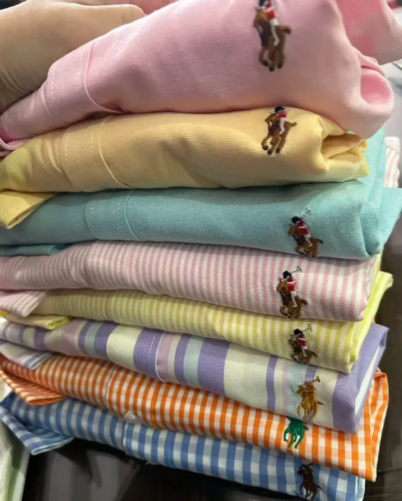 Stack of plain, striped and checked shirts in pastel colours with small embroidered motifs