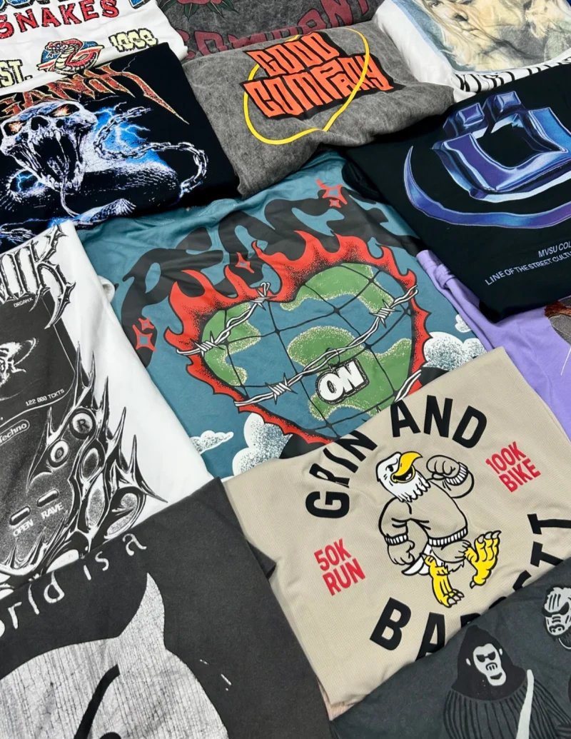 Folded T-shirts with globe and cartoon bird illustrations and lettering on different coloured backgrounds